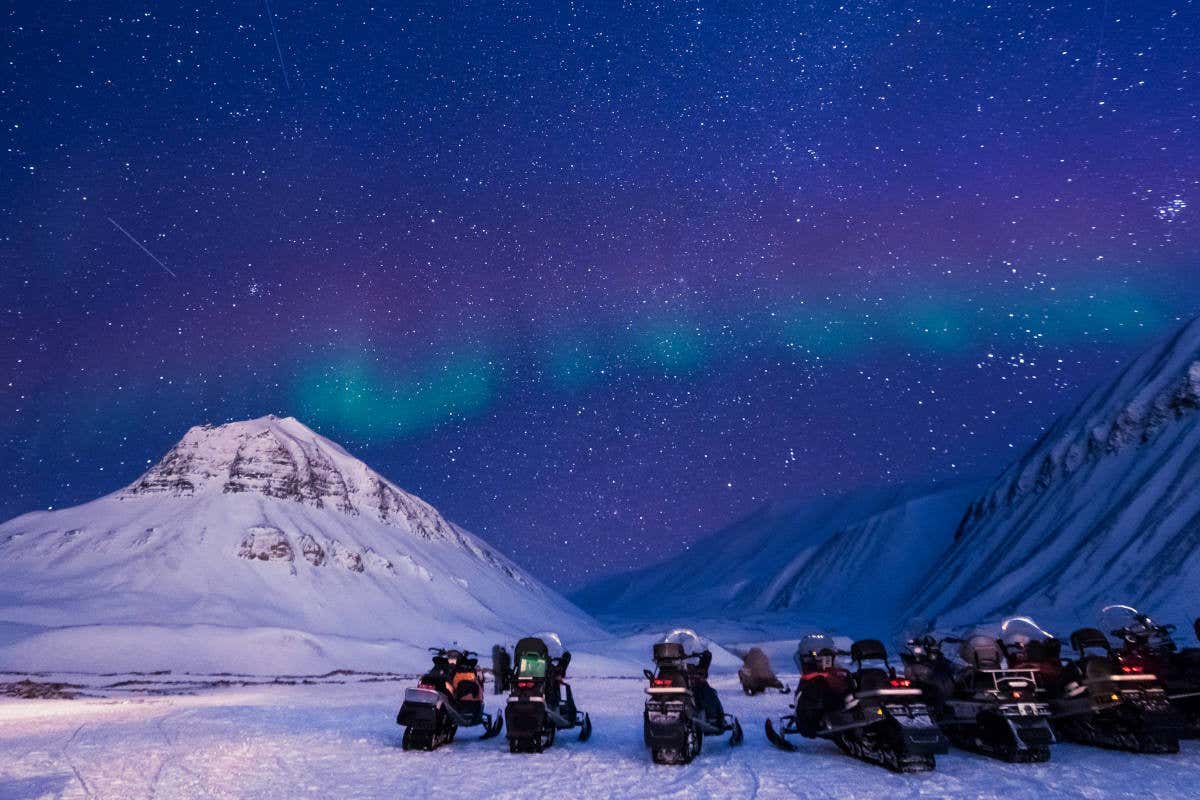 Motoslitte ferme in una vallata sotto un cielo stellato con aurora boreale
