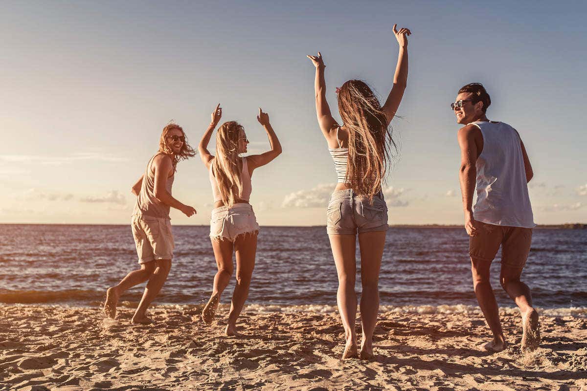 Cuatro personas jóvenes levantando los brazos durante la celebración del Ferragosto en una playa italiana