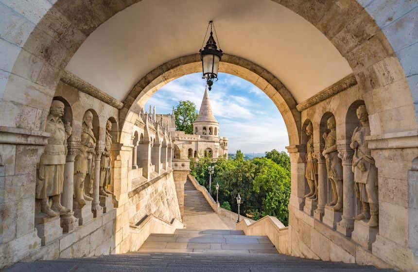 Uma escadaria que leva a um túnel de pedra com 3 esculturas de guerreiros de cada lado e um castelo ao fundo 