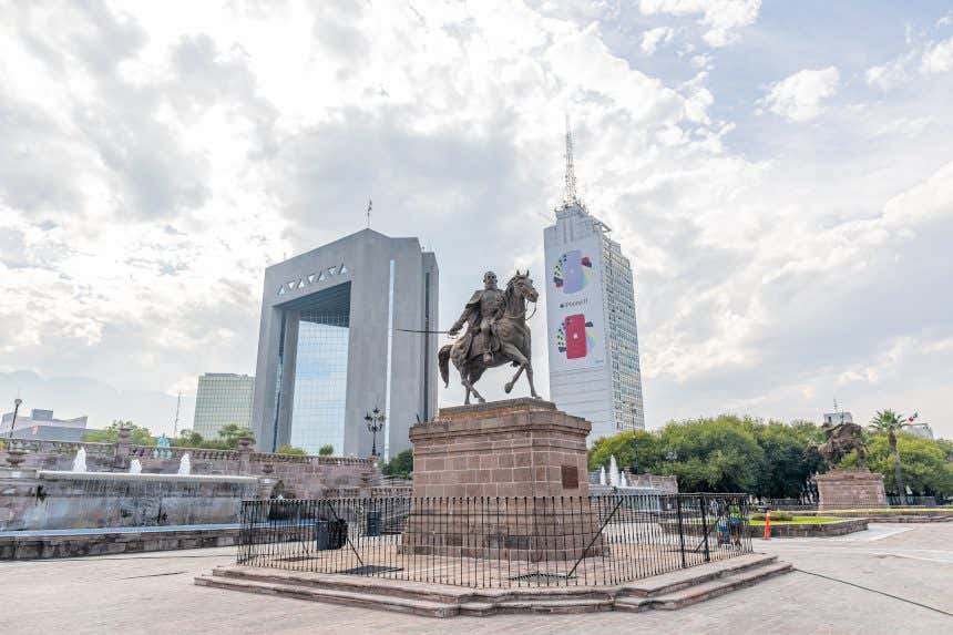 Estátua equestre no centro da Macroplaza de Monterrey, no México, com edifícios ao fundo