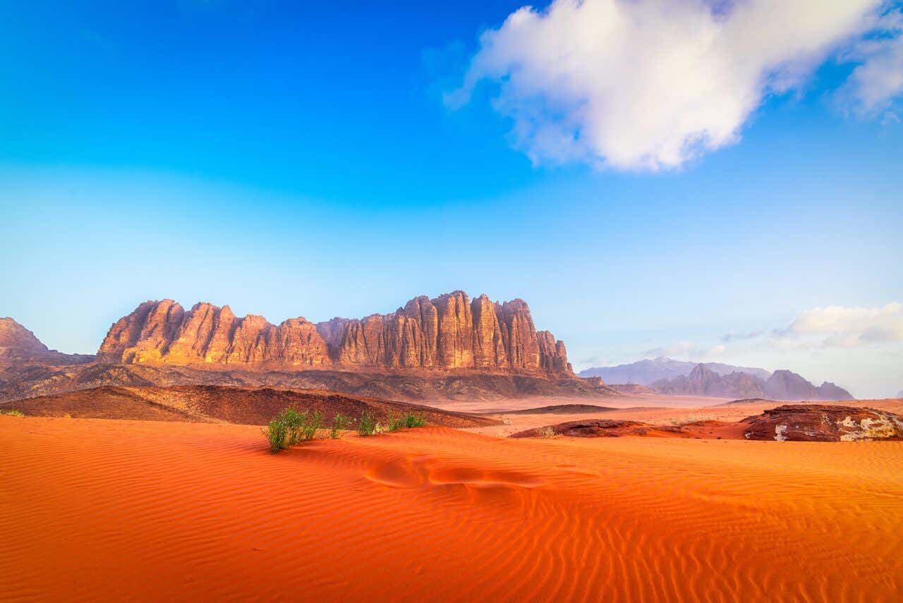 Désert orange du parc naturel de Wadi Rum avec des falaises en arrière plan et un ciel bleu