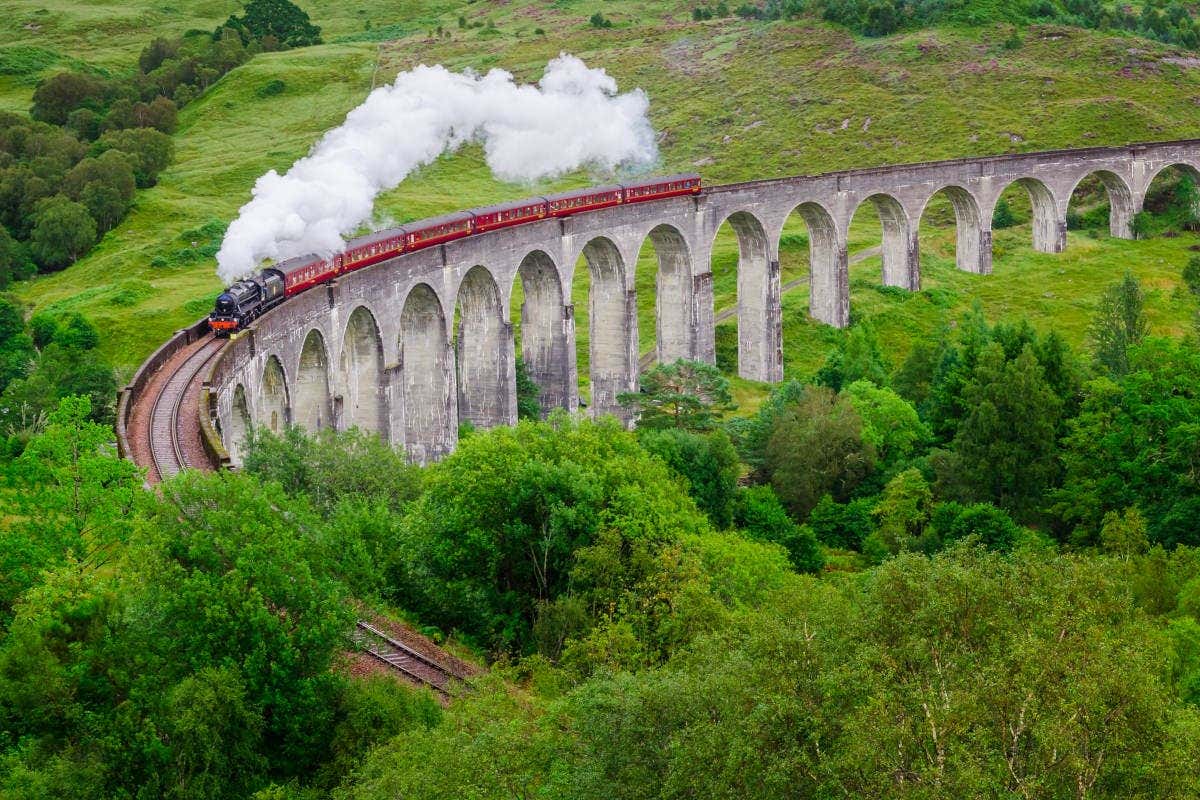 Locomotora a vapor pasando por el Viaducto de Genfinnan junto a bosques verdes