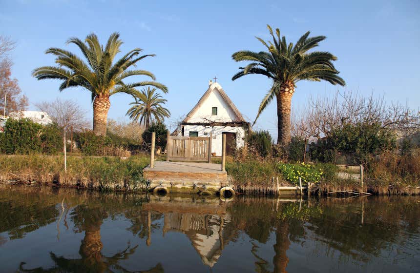 Embarcadero y una casa blanca de tejado triangular junto a dos palmeras en la Reserva Natural de La Albufera, en El Palmar.