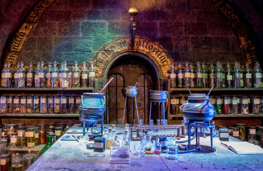 Flacons en verre et chaudrons sur une table de la salle de cours de potions d'Harry Potter avec des bocaux en arrière-plan