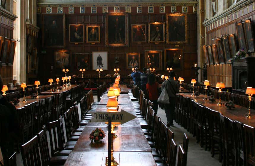 Des visiteurs parcourent la grande salle contenant des tables et des tableaux au Christ Church College, à Oxford