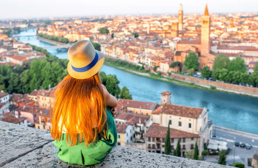 A girl with a straw hat looking at views of the city from the Adige river.