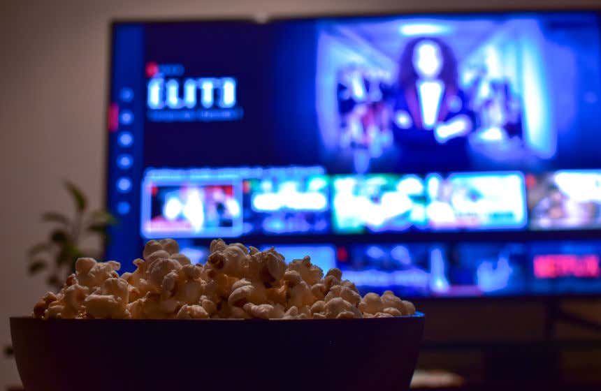 Cuenco de palomitas en primer plano y, de fondo, una pantalla de televisión con el catálogo de series de Netflix y Élite en emisión.