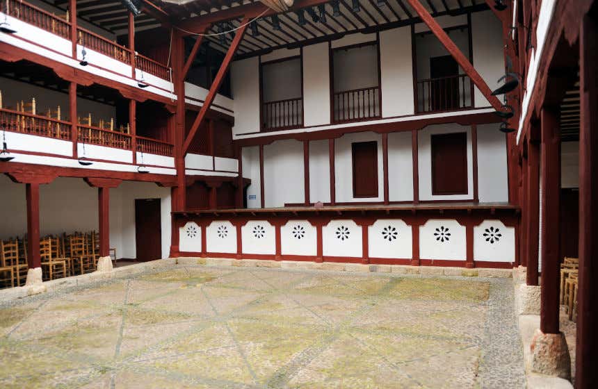 Vista del corral de comedias de Almagro con sus columnas y vigas de madera y sus tonos blancos y rojizos con las sillas a ambos lados.