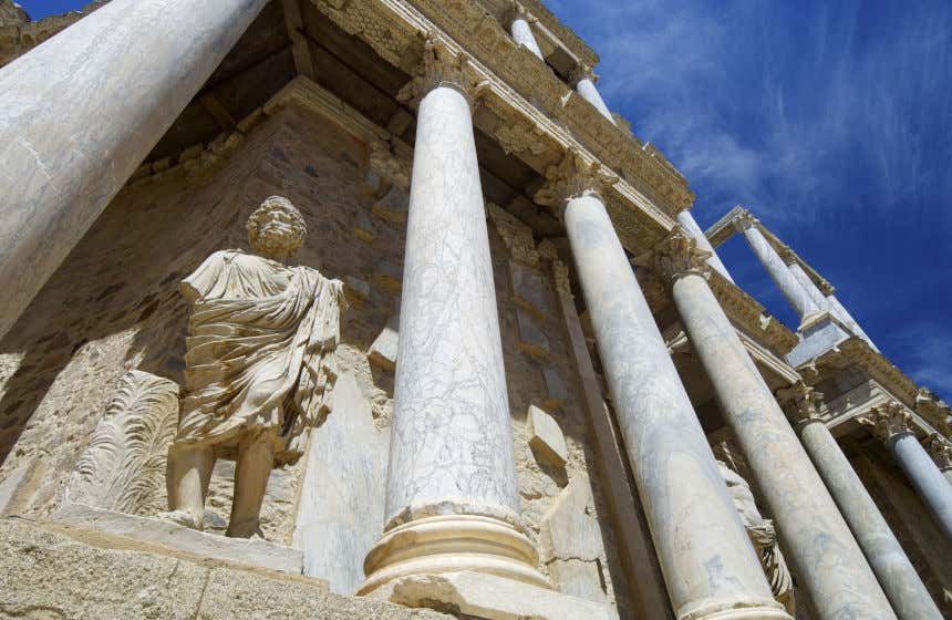 Una escultura romana de un varón con túnica junto a columnas corintias en el Teatro Romano de Mérida.