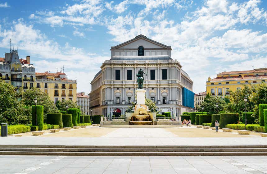 Monumento a Felipe IV frente a la fachada del Teatro Real de Madrid en una escena rodeada por edificios y setos.