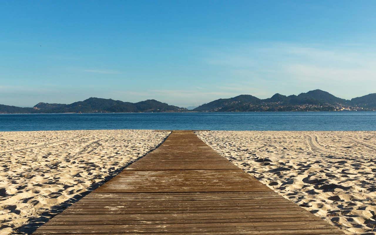 Uma faixa de madeira entre a areia da praia que leva até o mar da praia de O Vao