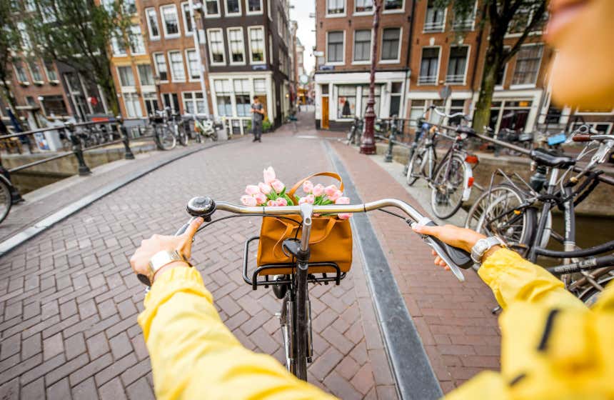 Vista de las manos de una joven subida en una bicicleta atravesando un puente de Ámsterdam.