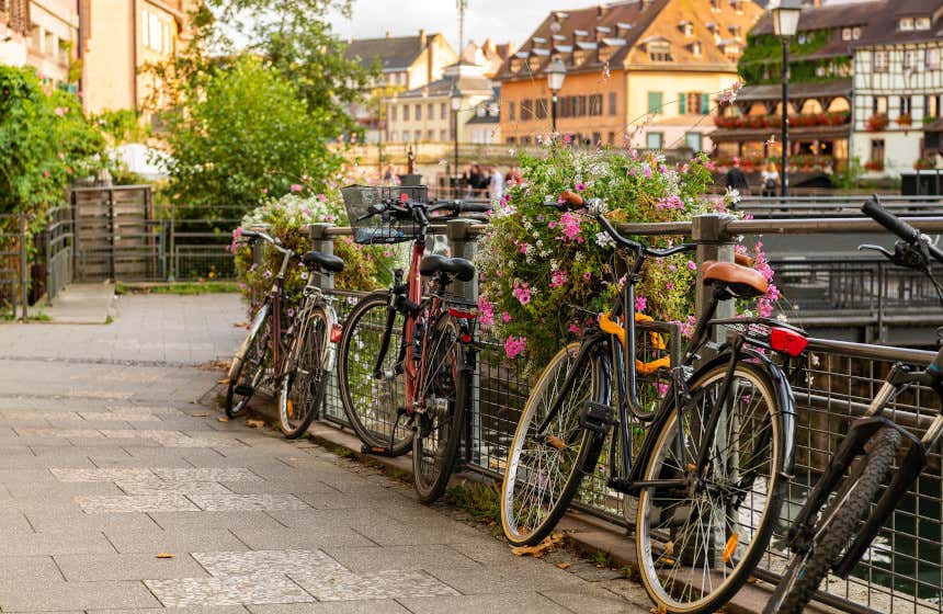 Cuatro bicicletas aparcadas junto a pun puente con flores en Estrasburgo frente a unas casas que se ven al fondo.
