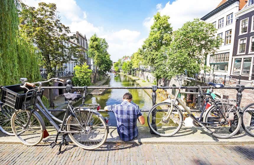Un joven sentado en un puente de Utrecht junto a dos bicicletas.