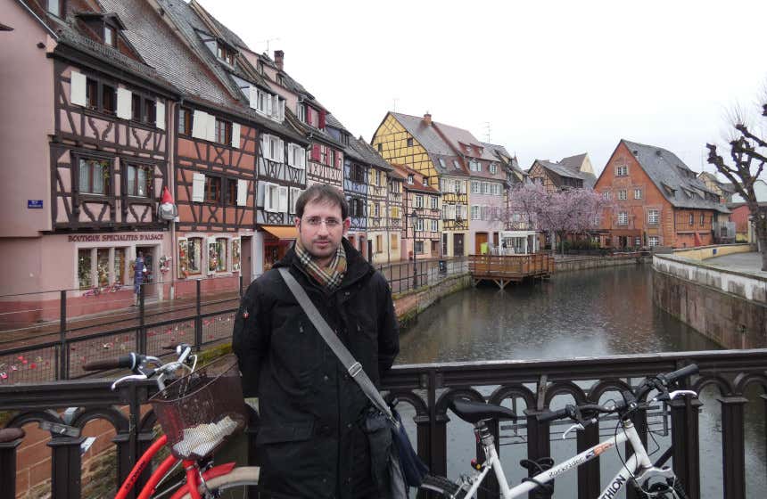 Javier Alameda, content copywriter de Civitatis, visitando la ciudad de Colmar, conocida como la pequeña Venecia de Alsacia. Fotografía tomada en un puente frente a uno de los canales con las coloridas casas con detalles de madera al fondo.