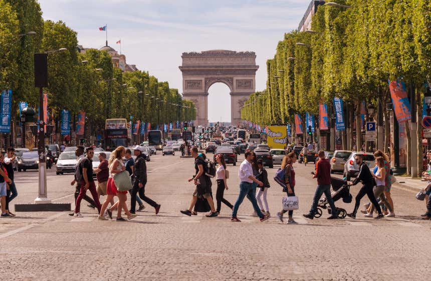 Un grupo de personas cruzan por una paso de peatones en la avenida de los Campos Elíseos. Al fondo, se divisa el famoso Arco del Triunfo.