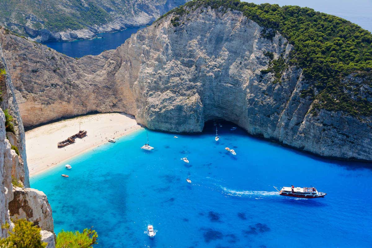 Vista aérea del naufragio en la playa Navagio, con varios barcos llegando a la costa en un día soleado 