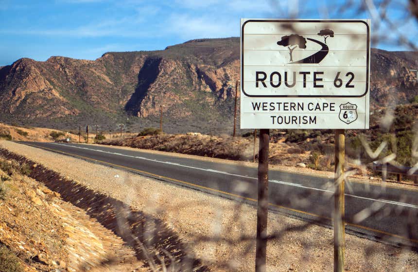 Cartel de la Ruta 62, una de las carreteras más turísticas de Sudáfrica. Al fondo, vista de varias montañas con vegetación.