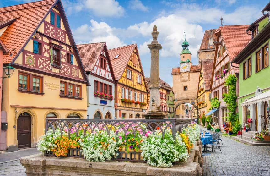 Casas de tejados triangulares y fachadas de colores en una plaza junto a una fuente con flores en Rotemburgo.