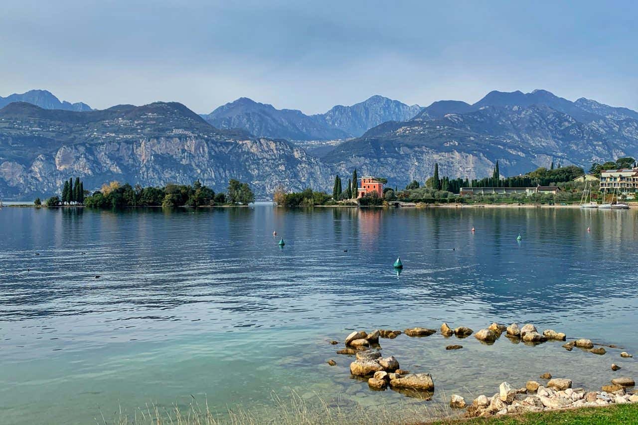 Lago di Garda, uno dei laghi più belli d'Italia, con le montagne e gli alberi sullo sfondo.