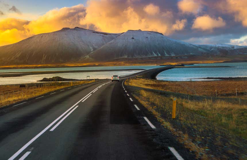 Carretera Ring Road de Islandia con un coche atravesando la ruta en mitad de un lago frente a unas altas montañas.