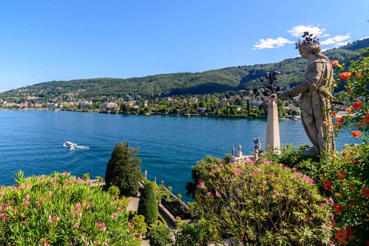 Il Lago Maggiore, uno dei laghi più belli d'Italia, con una statua a dominare la vegetazione e lo specchio d'acqua e una barca che naviga per le sue acque.