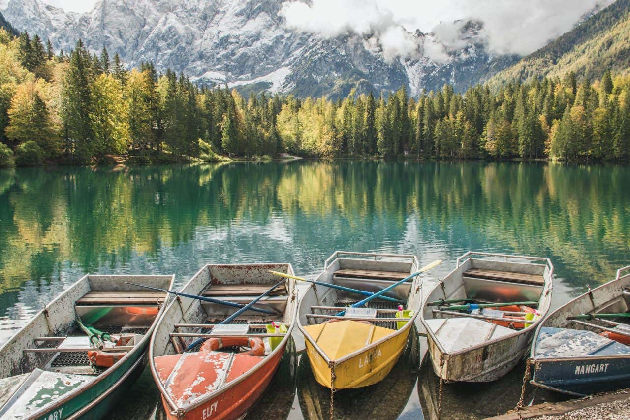 Barche a remi sulla riva dei laghi di Fusine, con gli alberi e il monte Mangart a fare da sfondo.