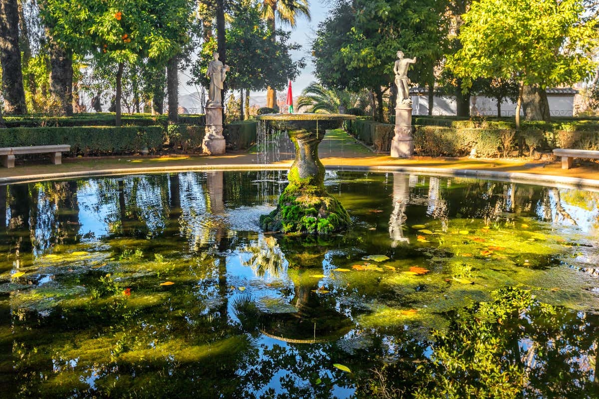 Une énorme fontaine pleine de végétation face à deux sculptures humaines dans les jardins de Carmen de los Mártires, à Grenade