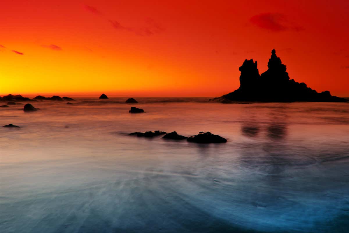 Mar en calma y cielos anaranjados al atardecer frente a los roques volcánicos de la playa de Benijo, en Tenerife.