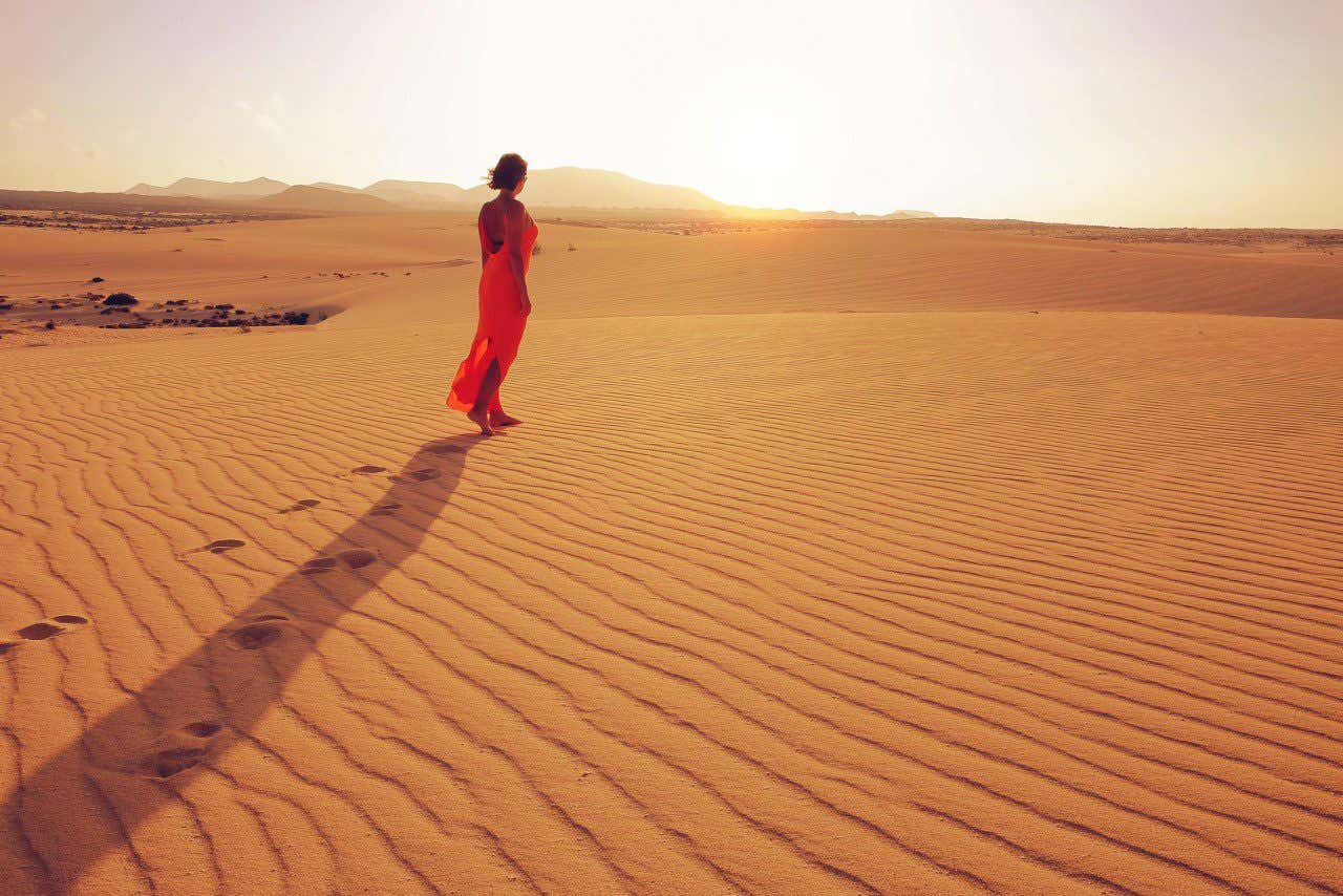 Una mujer con un vestido rojo camina sola por las dunas de arena de la playa de Corralejo, en Fuerteventura.