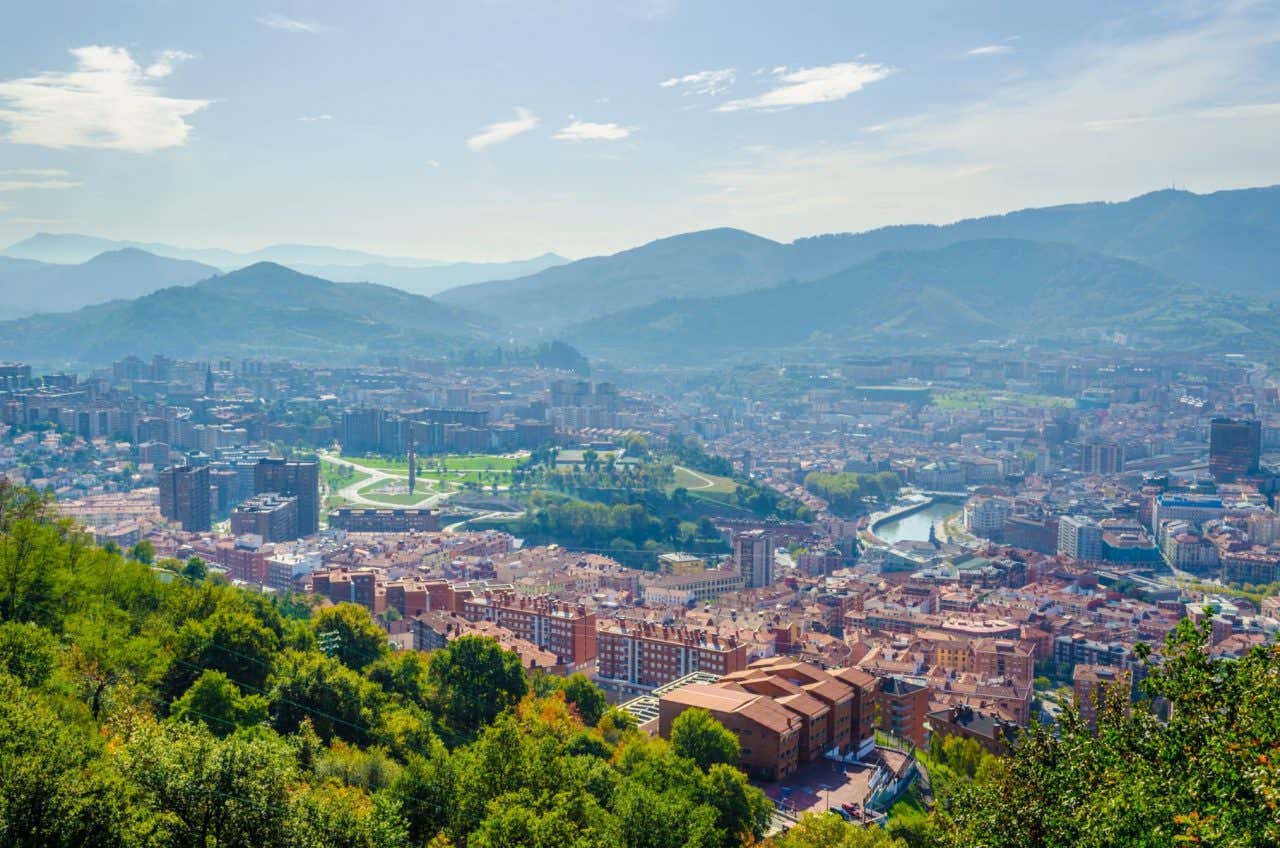 Views of Bilbao from Mount Artxanda, showing dense urban areas and green spaces, as well as mountains in the background