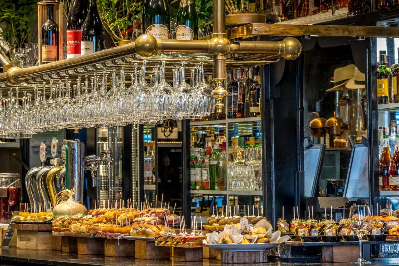 A shot of a bar filled with various traditional pintxos and drinks and glassware in the background