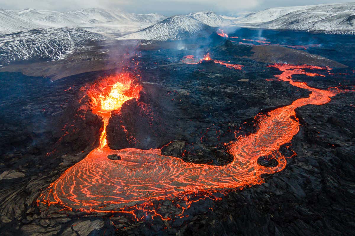 Montanhas nevadas perto do vulcão Fagradalsfjall da Islândia enquanto a lava flui pela sua cratera e arredores