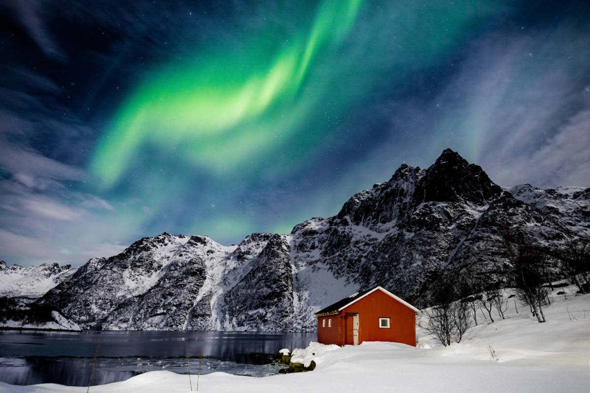 Una casa roja junto a las montañas de Svolvær bajo la aurora boreal