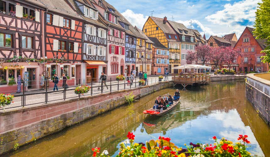 Canali di Colmar, uno dei luoghi da vedere in Alsazia, con una piccola barca e dei turisti a bordo che ammirano le casette colorate.