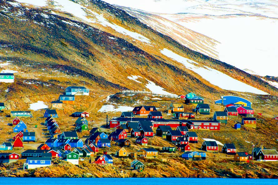 Ittoqqortoormiit full of colourful houses on a mountain side, near a body of water with snow on the tops of the mountain