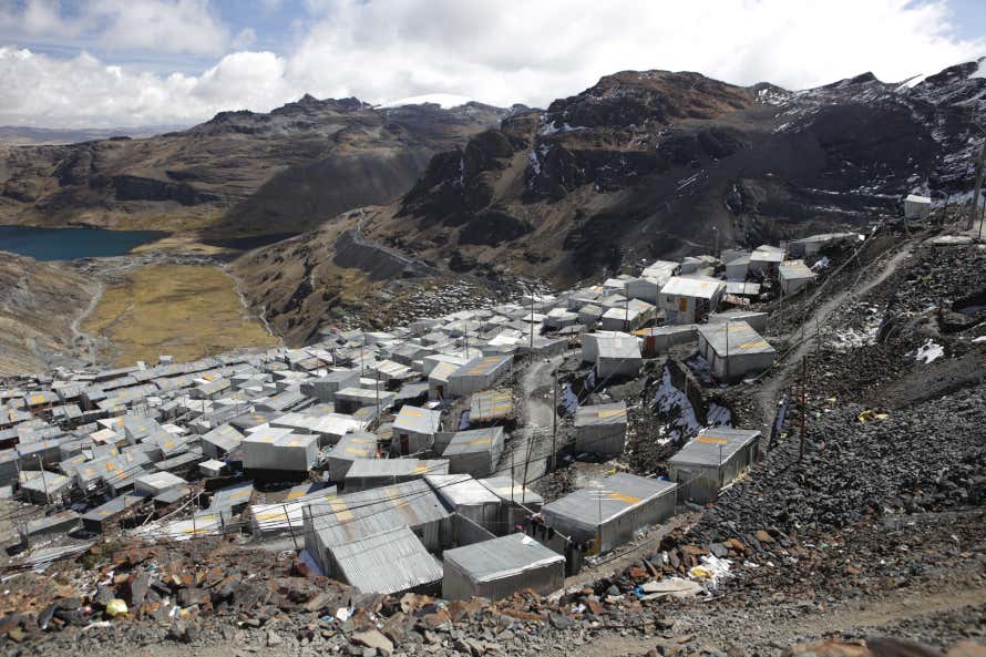 La Rinconada, Peru, with grey houses in close proximity to each other on a mountain side with a lake nearby