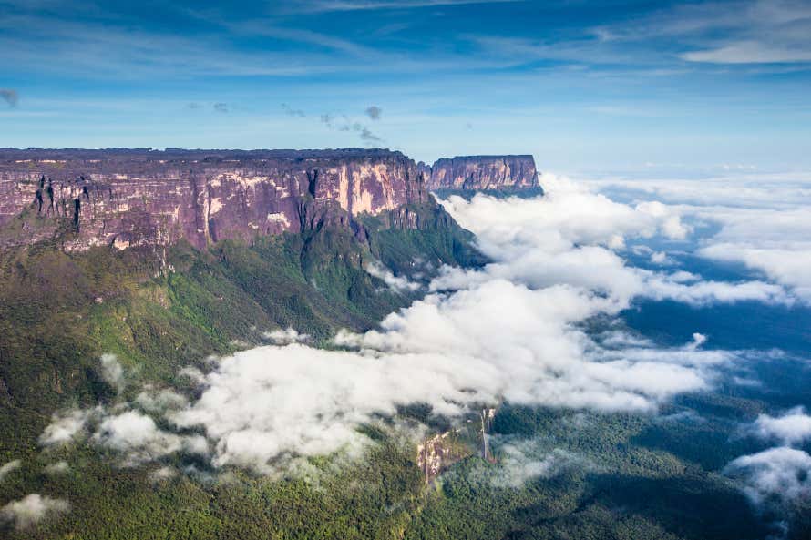 A view of Tepuy Roraima with white fluffy clouds and a clear blue sky