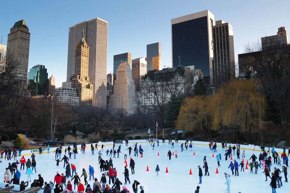 Decenas de personas patinando en la pista de hielo de Central Park frente a los altos rascacielos de Manhattan al fondo