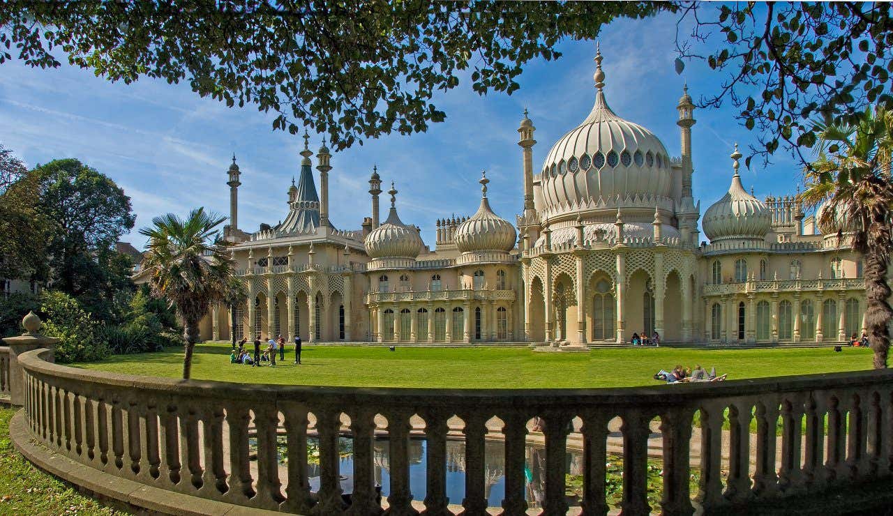 A picture of the Royal Pavillion in Brighton, on a sunny day with some people lying on the grass.