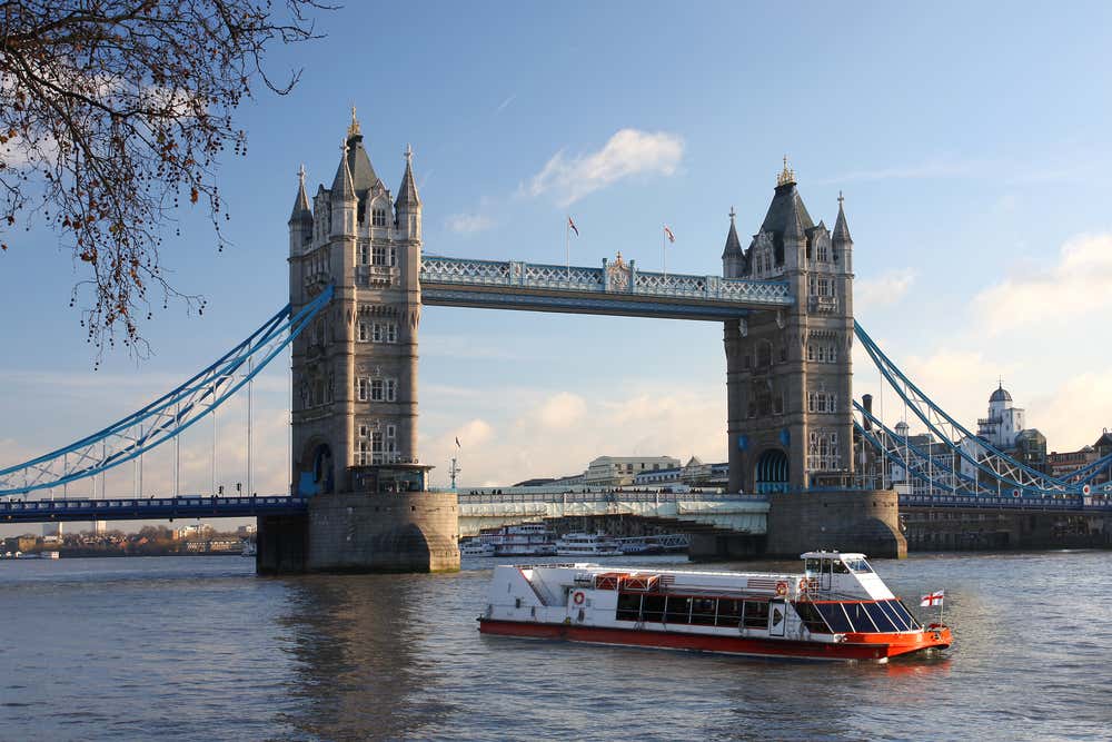 Tower Bridge, London, on a clear day, with a red and white boat sailing along the water.