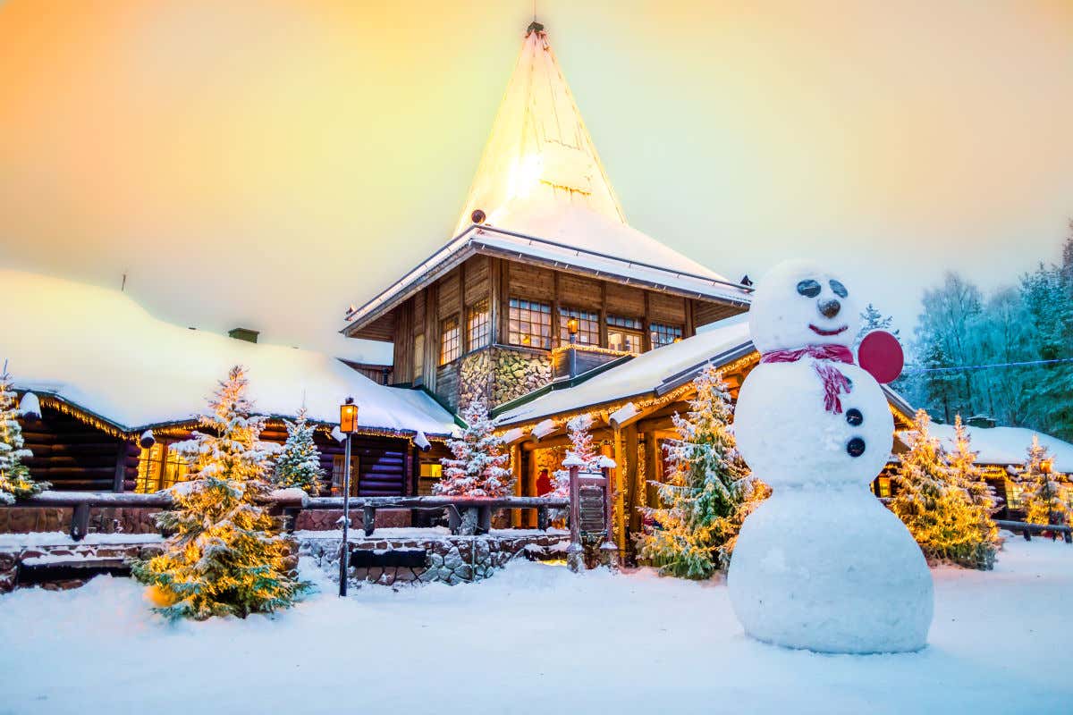 Casa de tejados nevados en la aldea de Papá Noel en Laponia. En los exteriores del edificio se pueden ver hasta ocho árboles de Navidad con luces y un muñeco de nieve.