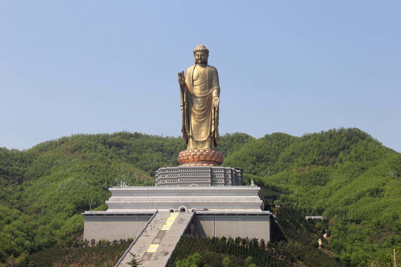 Imponente estátua de Buda no Templo da Primavera de Lushan, situada no alto de uma montanha e rodeada de árvores