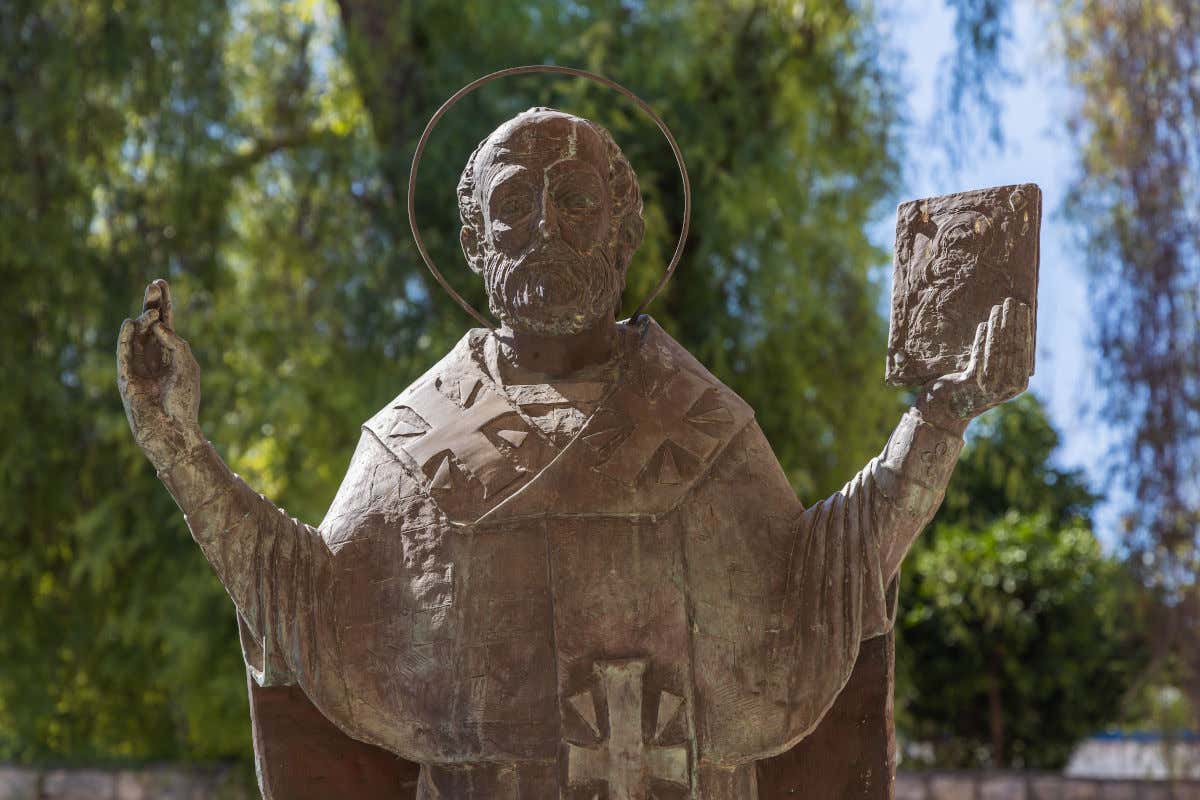 Estatua de bronce de San Nicolás con los brazos abiertos sosteniendo un libro en una de sus manos.