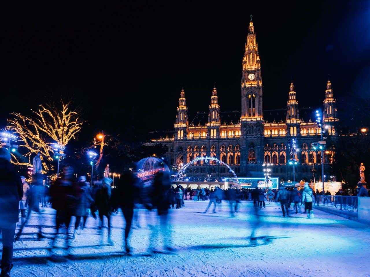 Vienna Ice Dream ice rink full of people ice skating around the rink, in front of the beautiful city hall.