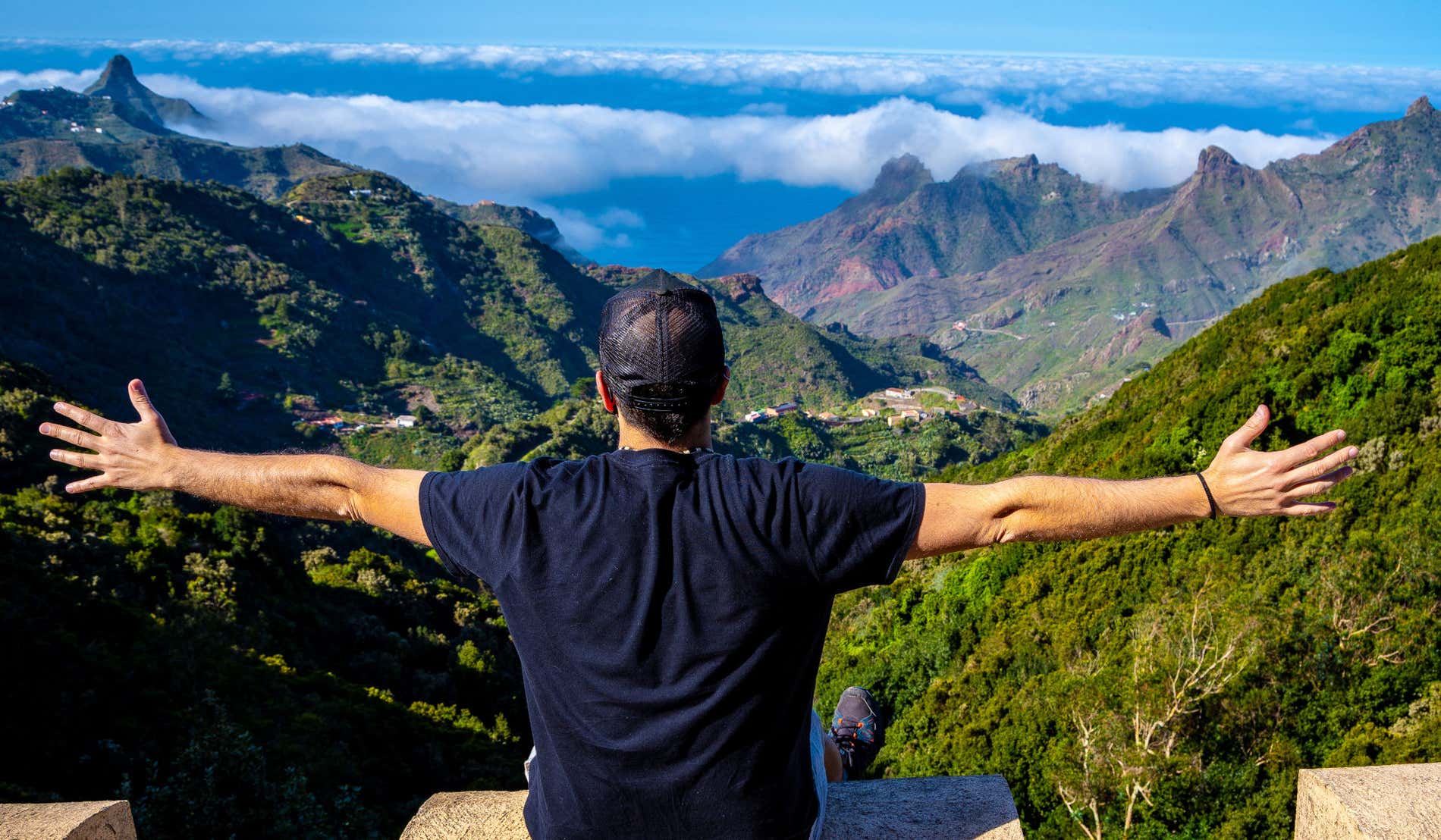Un hombre sentado de espaldas a la cámara frente a las montañas verdes del Parque Rural de Anaga, en Tenerife.