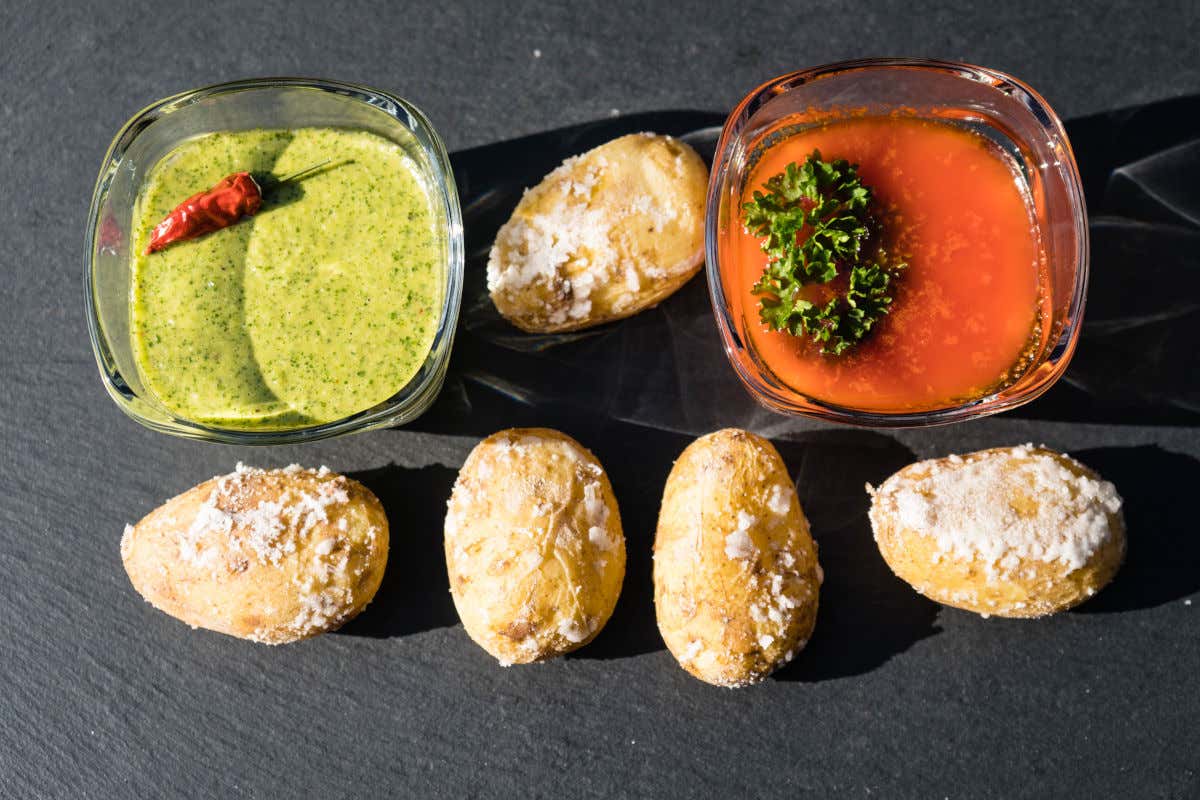 Papas arrugadas junto a dos cuencos de cristal con mojos verde y rojo típicos de la gastronomía canaria.