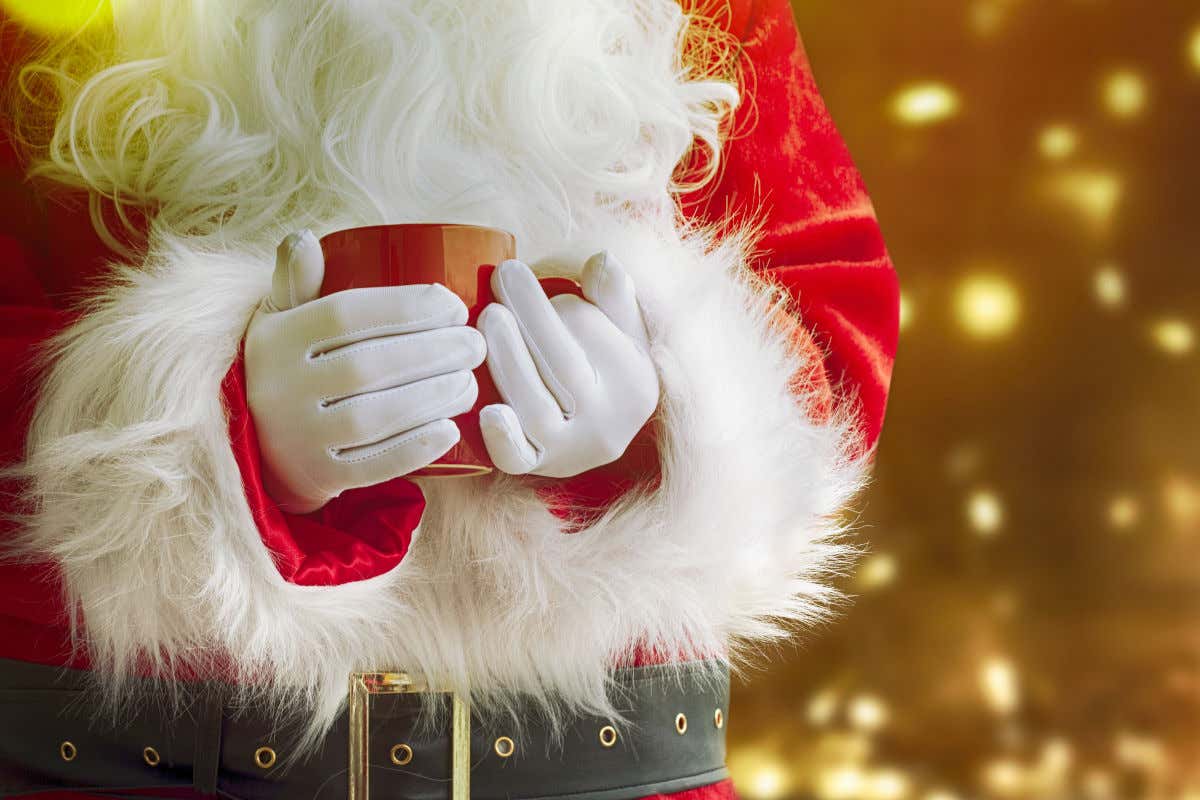 Vista de medio cuerpo, de cintura a hombros, de Papá Noel ataviado con guantes y sujetando una taza roja.