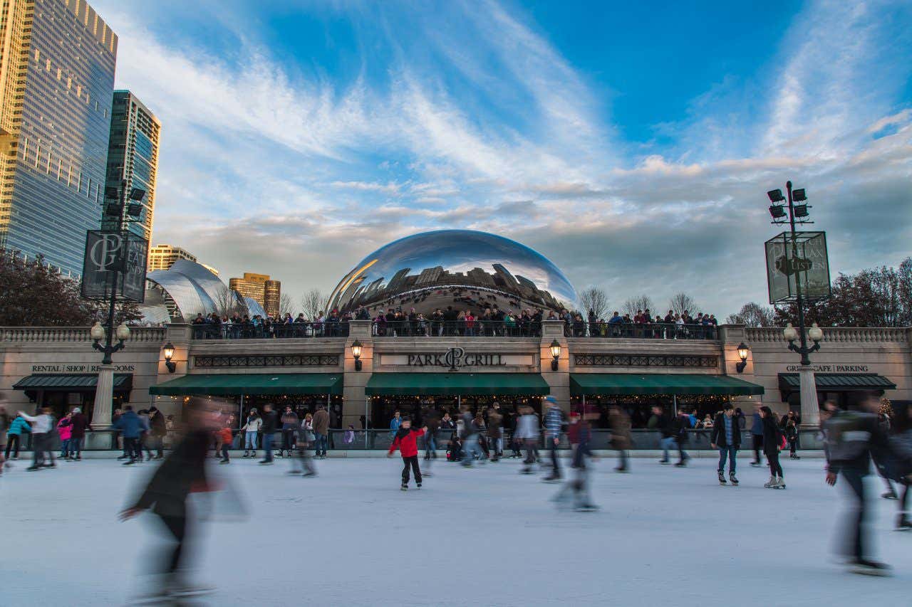 A picture of McCormick Tribune Ice Rink with people skating by, and a blue sky and whispy white clouds above them.