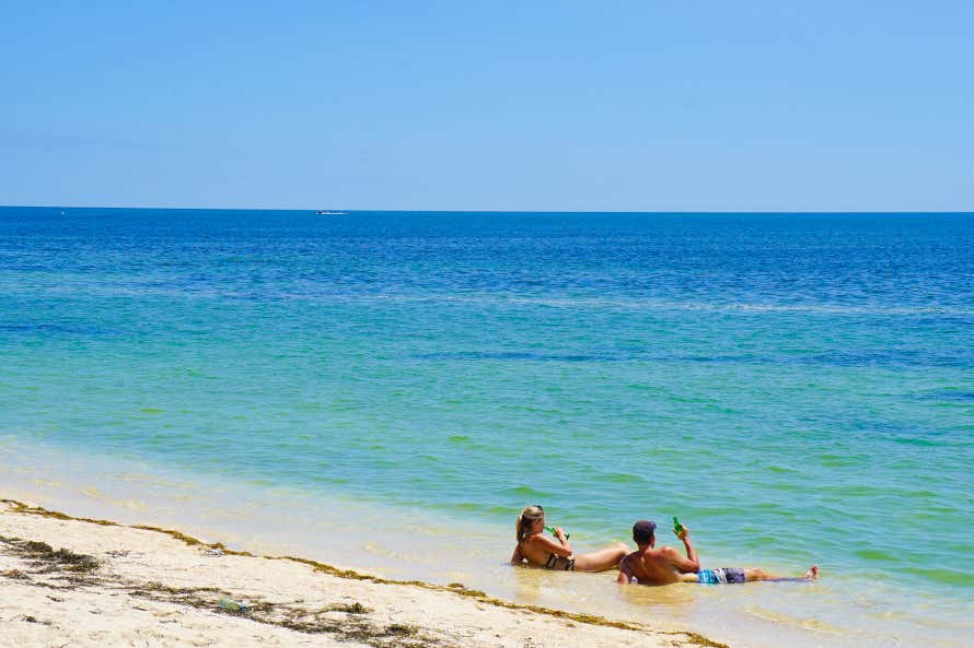 Casal descansando e tomando algo deitado na areia da praia de Ancón